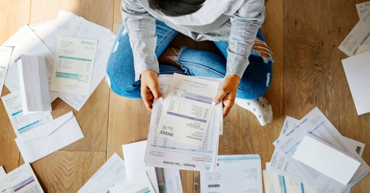Person surrounded by dozens of bills and invoices on the ground