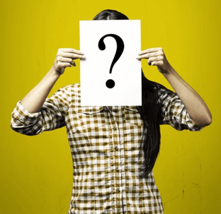 Woman in a checkered shirt holding up a "?" sign in front of her face