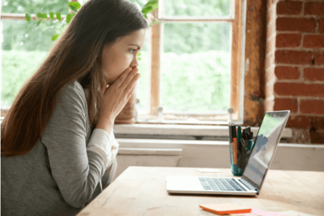 Worried woman looking at laptop with hands on her face