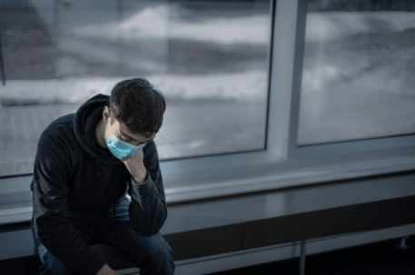Man with medical mask sitting with face in his hands