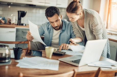 man and women with desk covered in paper work, calculator and laptop