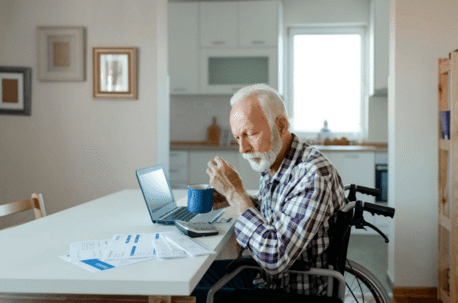 older man in wheelchair looking at documents with laptop