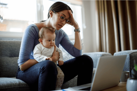 woman stressed holding baby looking at laptop