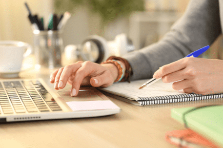 close up on woman's hand using laptop and writing in notepad