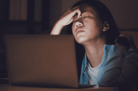 woman holding face over laptop in dark room