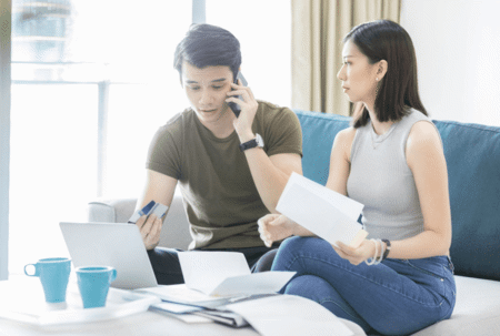 man and woman on couch holding phone, papers and credit card