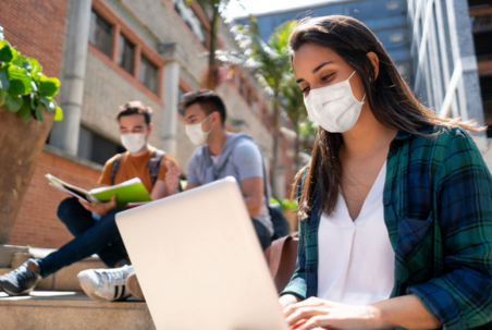 three students working on laptops with masks