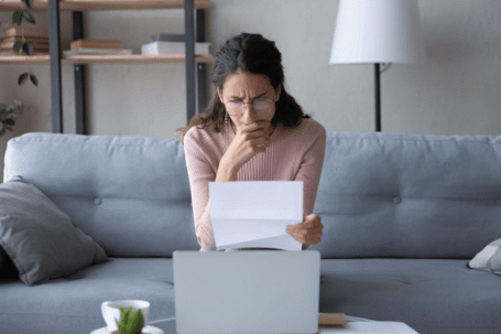 woman reviewing document on her couch with glasses and laptop
