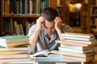 Man leaning face on hands while surrounded by stacks of books