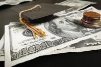 Stack of $100 dollar bills with coins and small graduation cap set on top