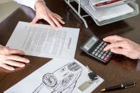 Two people reviewing paperwork and a calculator on a desk 