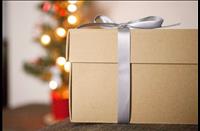Brown paper box wrapped with silver bow in front of blurred out holiday tree