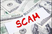 White paper with word " SCAM" written in red ink on top of $100 dollar bills