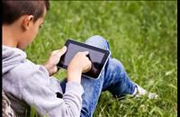Child on a tablet sitting in green grass