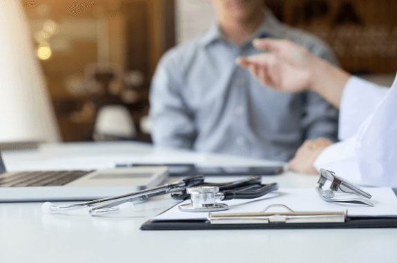 Coworkers sitting at a desk with a laptop, clip board, and a stethoscope