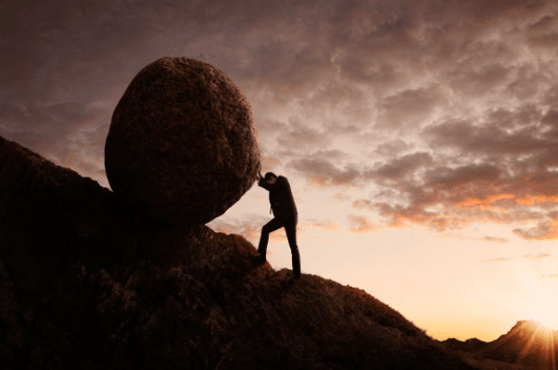 Person at sunset rolling a big bolder up a hill