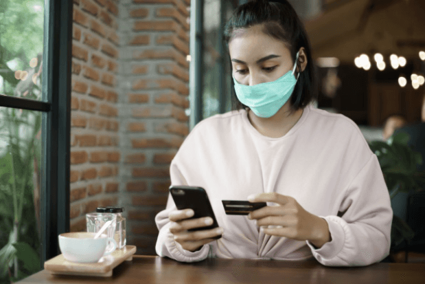 Woman in a coffee shop, holding a credit card and a cell phone