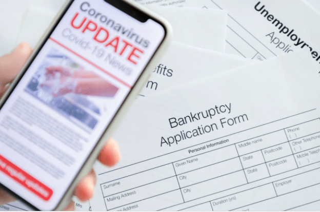 Coronavirus update on a cell phone that is held in front of a Bankruptcy Application Form