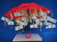 Red umbrella opened with dollar bills and coins hanging from the top