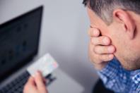 Man with hands covering his eyes while holding a credit card