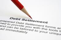 Red pencil pointing at "Debt Settlement" title on paper